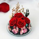 Detail čtyř stabilizovaných červených růží se zlatými sušenými květy uvnitř skleněného anděla